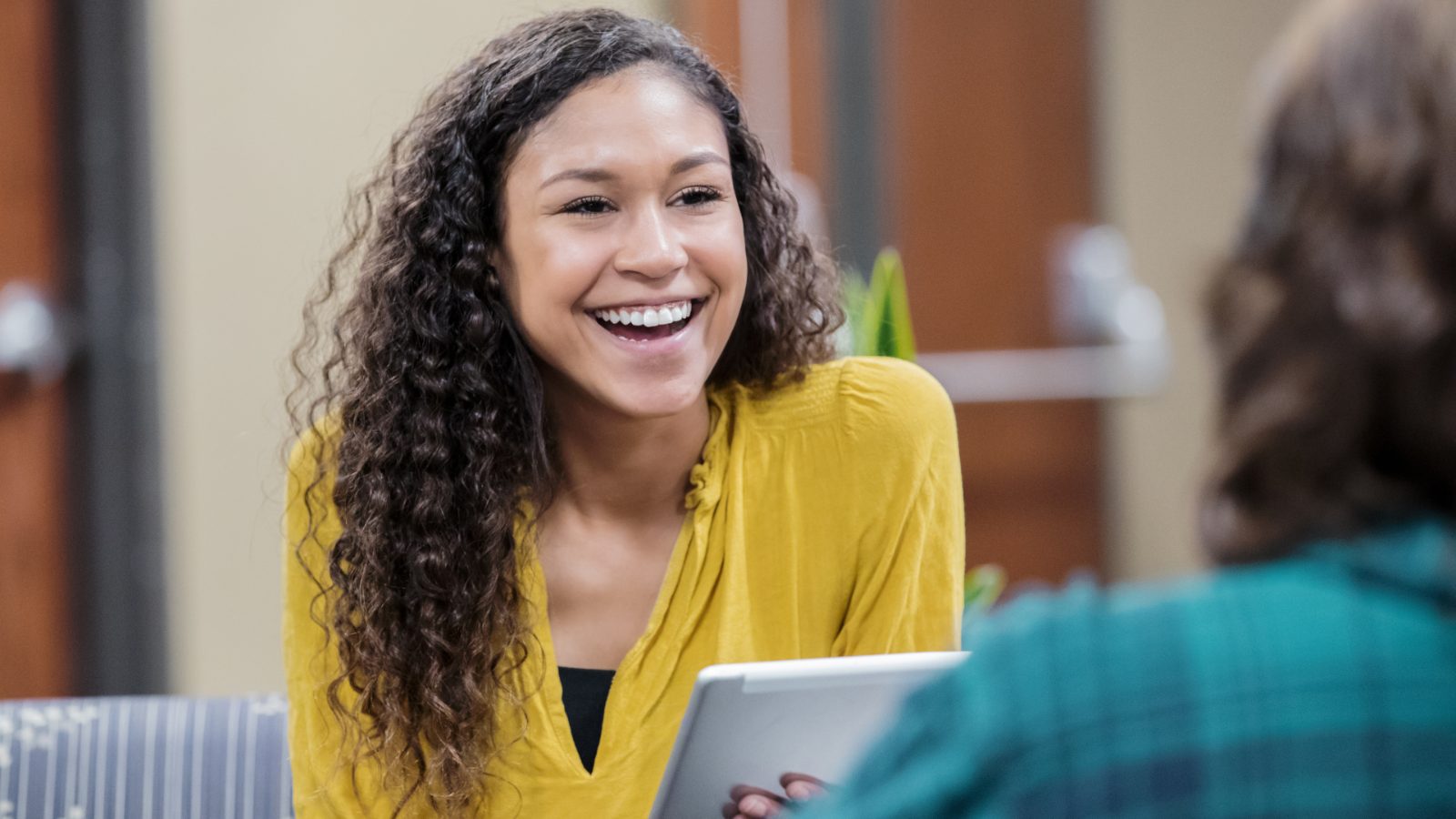 A woman smiling during a friendly conversation with a colleague who is making notes on a tablet